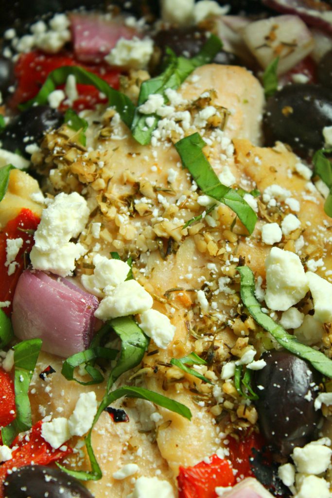 a lush, moist chicken breast in the bowl of a crockpot with fresh veggies including roasted red peppers and feta cheese