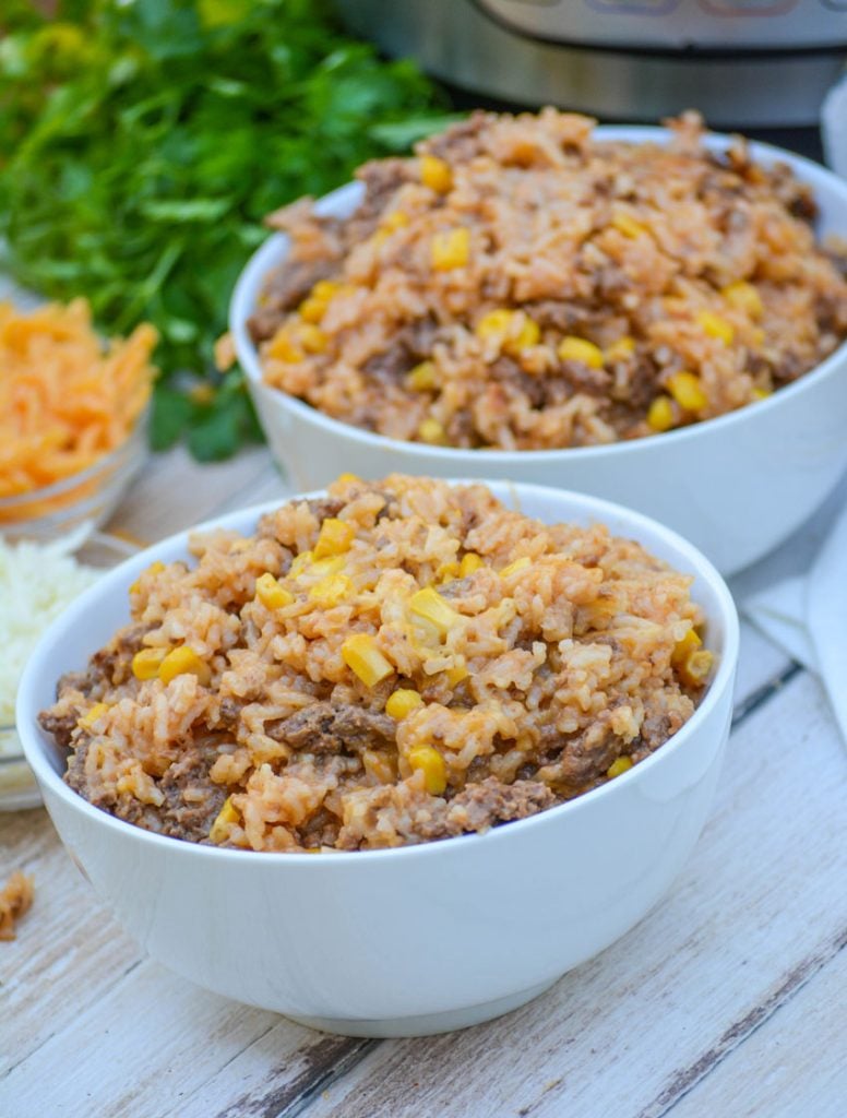 Instant Pot Cheesy Ground Beef & Rice shown in two white bowls with cheeses & Italian parsley in the background and a shiny Instant Pot there too