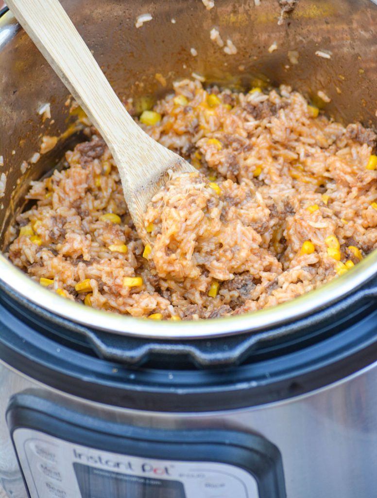 Instant Pot Cheesy Ground Beef & Rice pictured in the instant pot with a thick wooden spoon