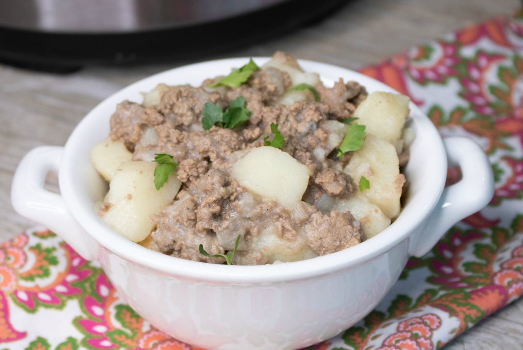 Instant Pot Ground Beef & Potato Hash is served in a white bowl with tiny handles on a floral patterned napkin