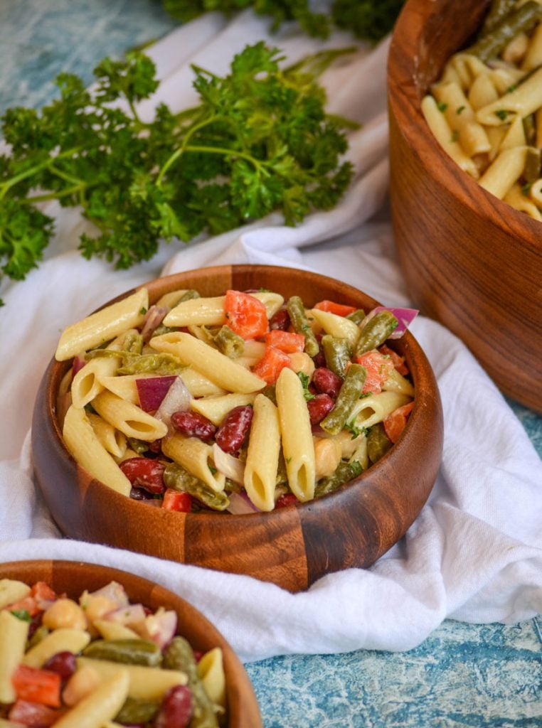 Three Bean Salad Pasta in a wooden bowl set on a white cloth with a bunch of fresh parsley in the background