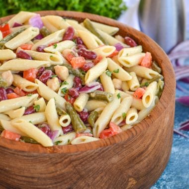 three bean pasta salad in a large wood mixing bowl with fresh herbs in the background