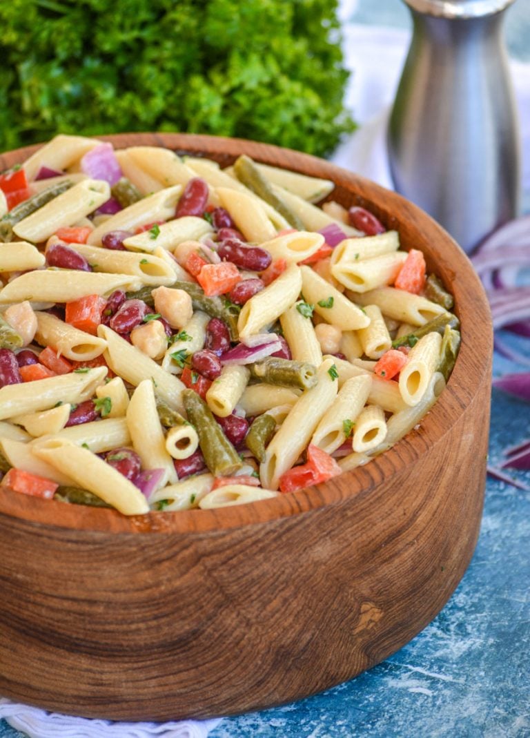 three bean pasta salad in a large wood mixing bowl with fresh herbs in the background