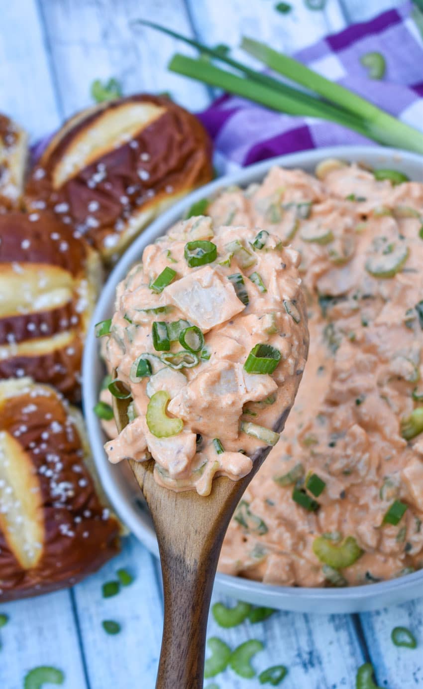 a wooden spoon scooping buffalo ranch chicken salad out of a gray serving bowl