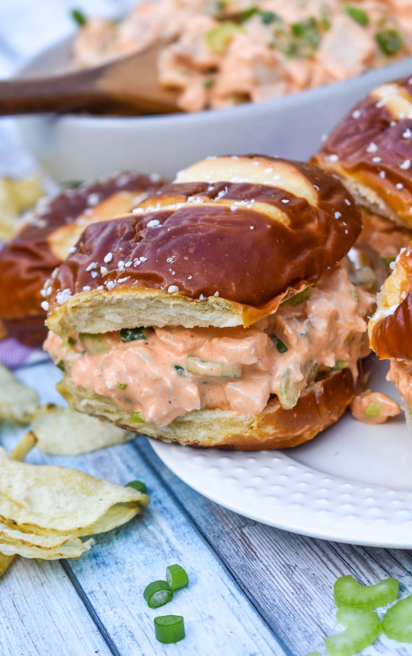 buffalo ranch chicken salad on a pretzel bun resting on the edge of a white plate