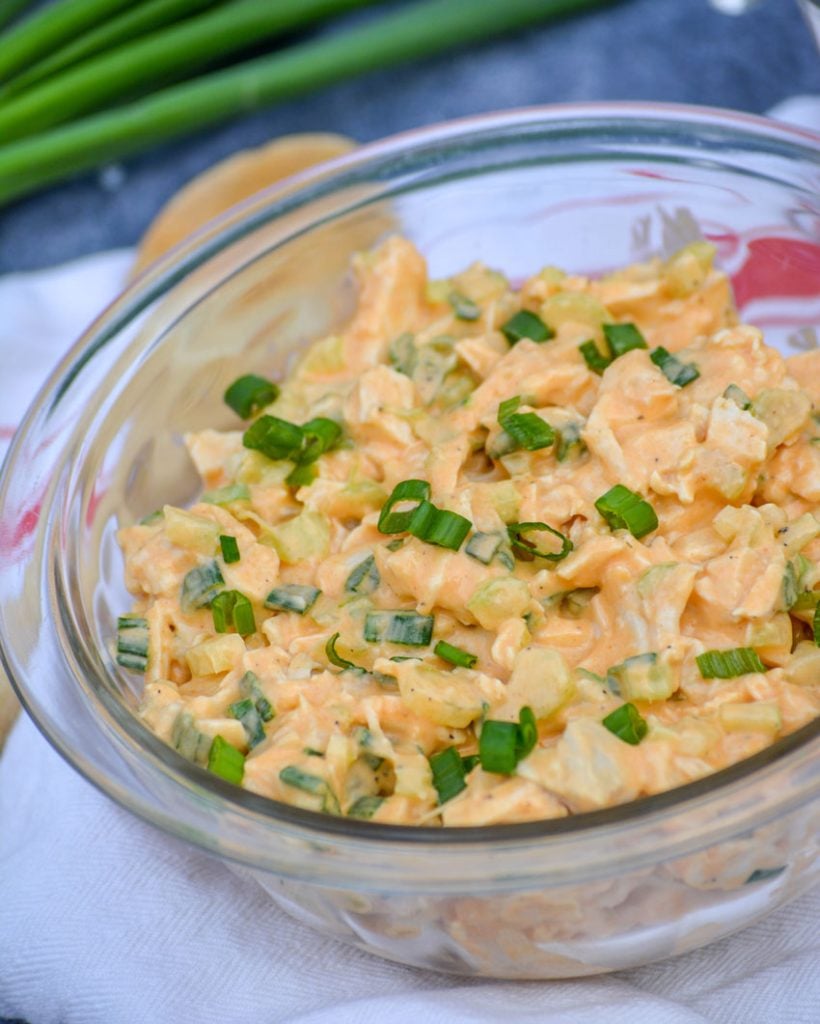 chicken salad in a creamy buffalo ranch sauce is in a glass bowl on a red & white dish towel and garnished with thinly sliced green onions