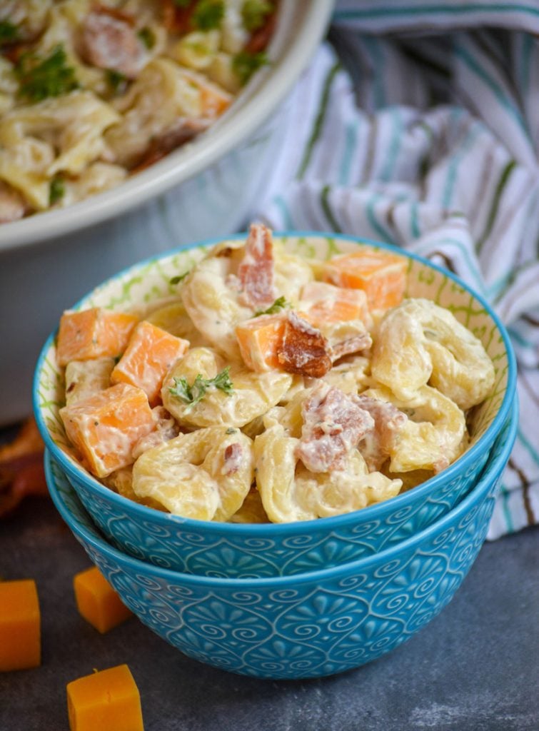 cold tortellini salad with ranch dressing in a stacked sky blue bowls is studded with cubes of cheddar cheese and crisp pieces of bacon