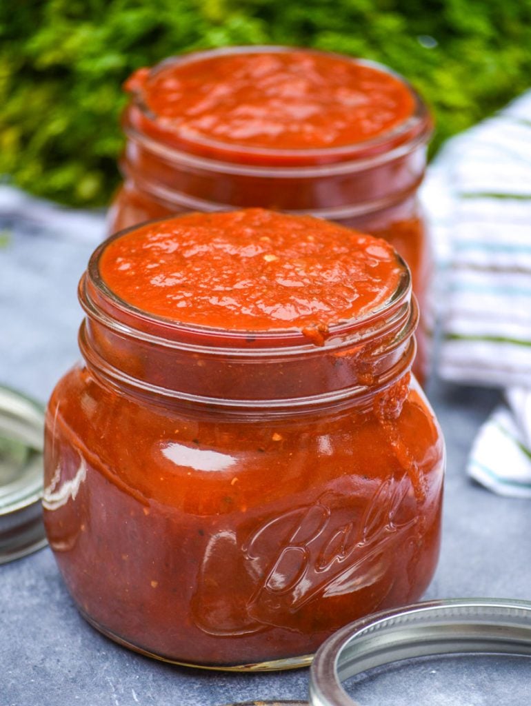 homemade marinara sauce in clear glass jars with lids and rings pictured and fresh parsley in the background