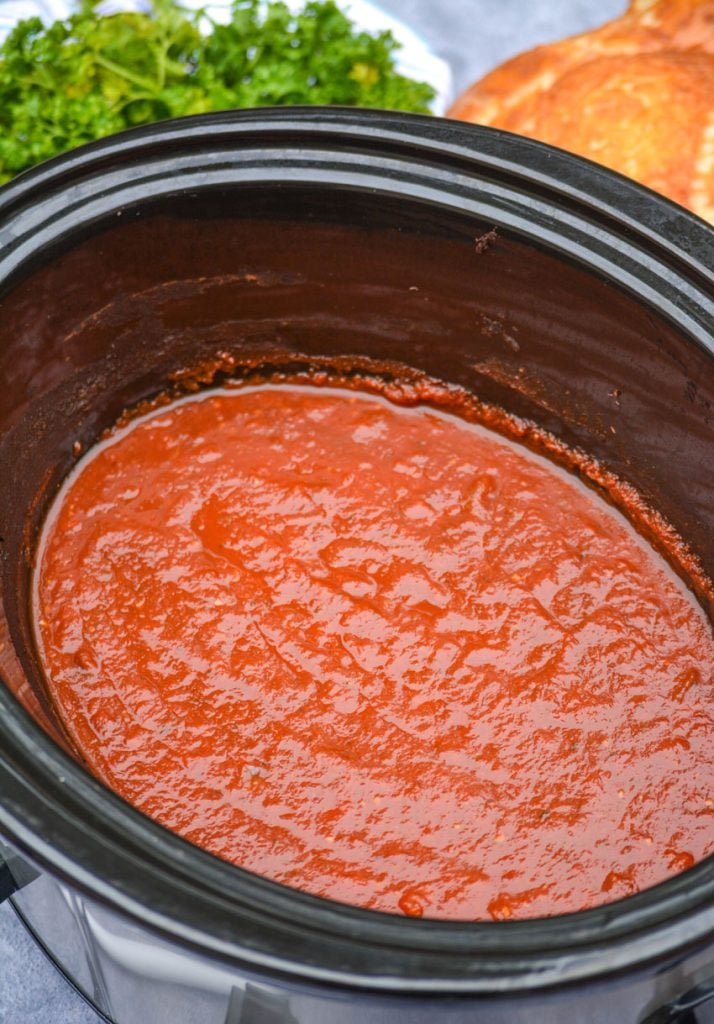 freshly made marinara sauce in the black crock of a slow cooker with parsley and bread in the background