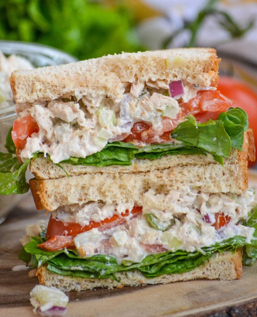 creamy dill pickle tuna salad is shown as a hearty sandwich cut in half, stacked, and studded with pickle chunks and bright red onion