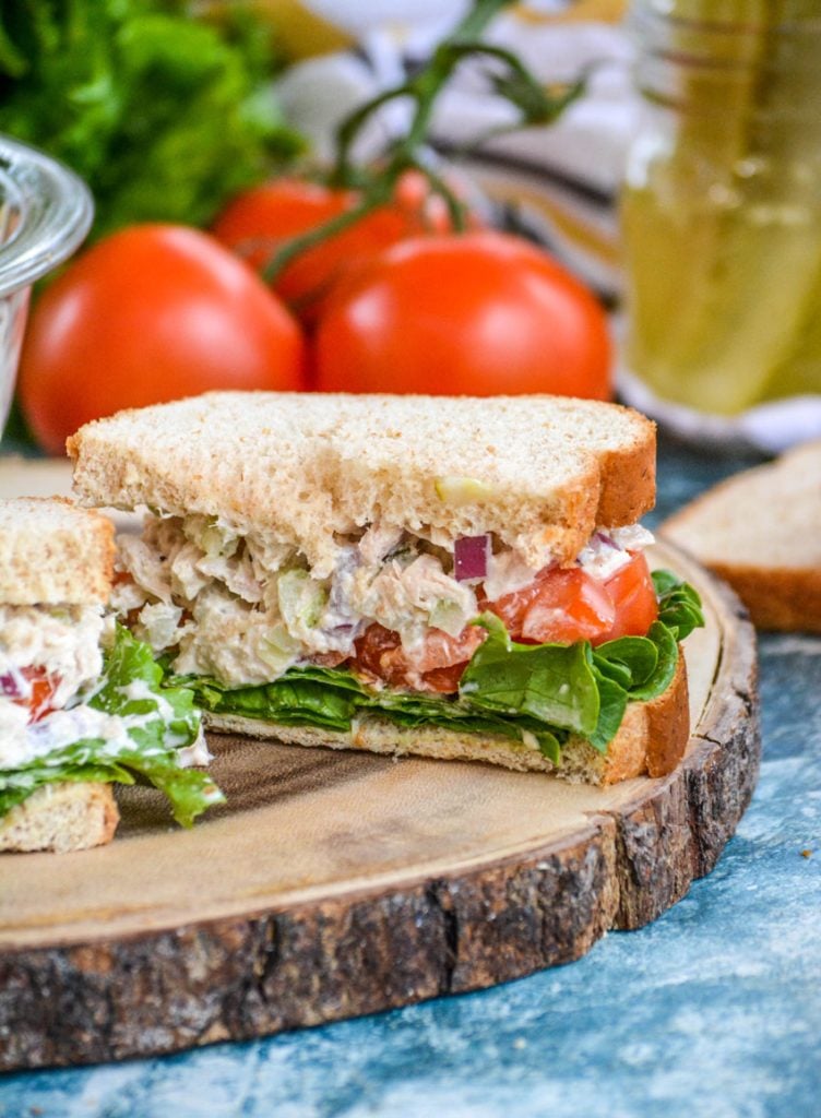 dill pickle tuna salad sandwich cut in half is shown with crisp lettuce and juicy tomato slices