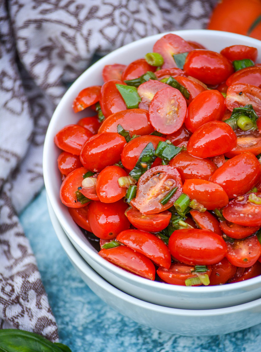 MARINATED TOMATO SALAD TOPPED WITH FRESH HERBS IN A WHITE BOWL