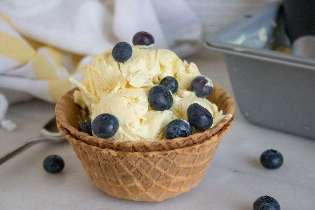 fresh blueberries top several scoops of bright yellow creamy homemade lemonade ice cream