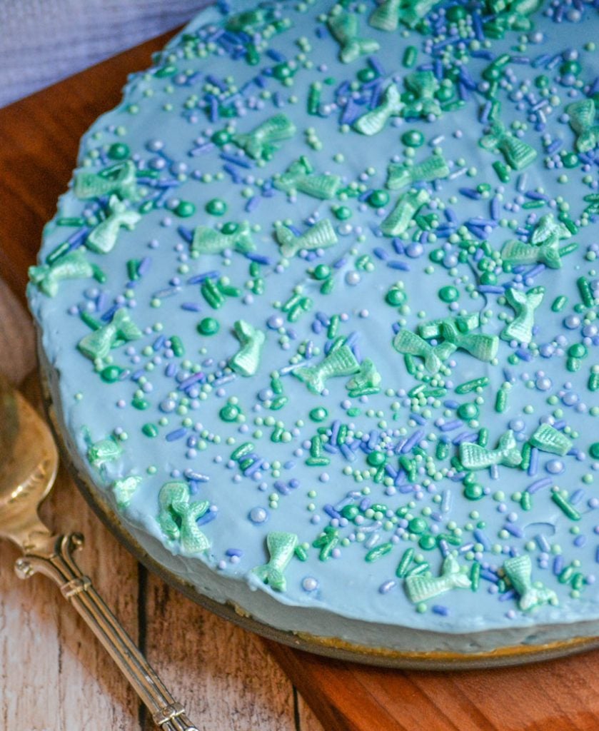 blue no bake mermaid cheesecake is topped with shinny sprinkles in dusky blue, teal, and sea foam green including ones shaped like mermaid's tails