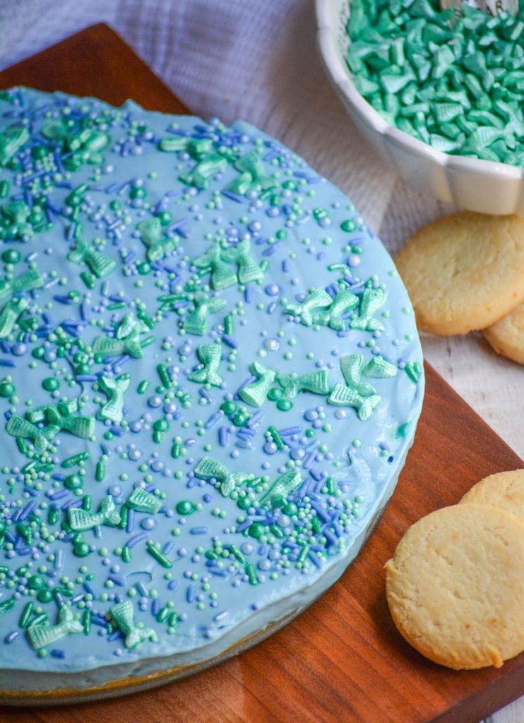 dyed blue, this no bake cheesecake is topped with a spinkle of green and blue hued sprinkles and largers sprinkles shaped like mermaids tails