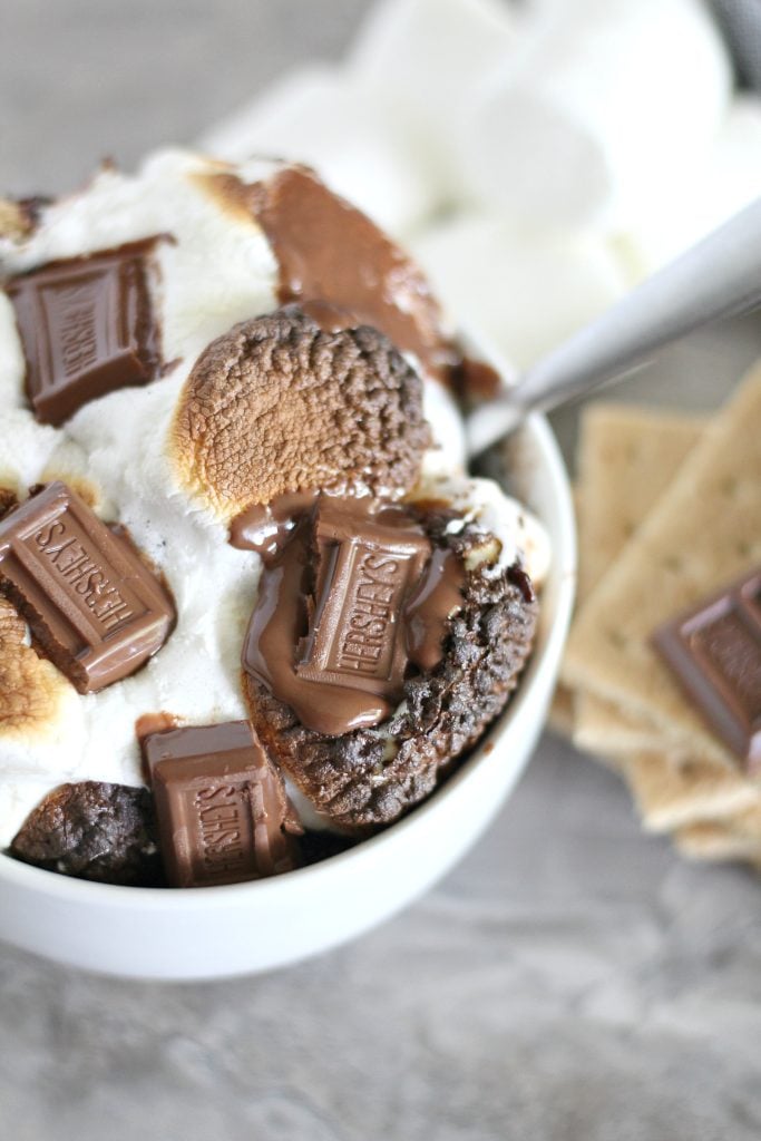 s'mores cobbler is in a white bowl loaded with toasted marshmallow bits and half melted mini hershey's candy bars