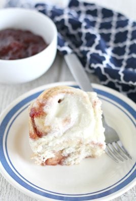 strawberry cinnamon roll on a blue rimmed white plate with a silver fork