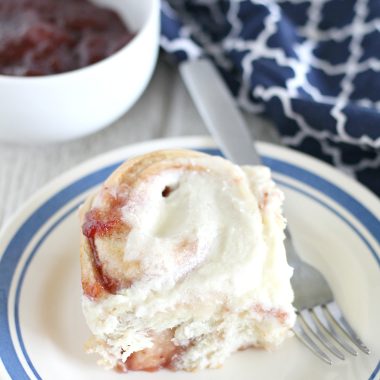 strawberry cinnamon roll on a blue rimmed white plate with a silver fork