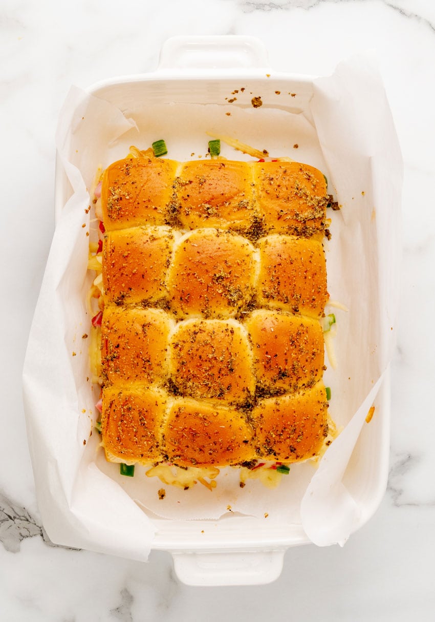 hawaiian pizza sliders in a parchment paper lined white baking dish