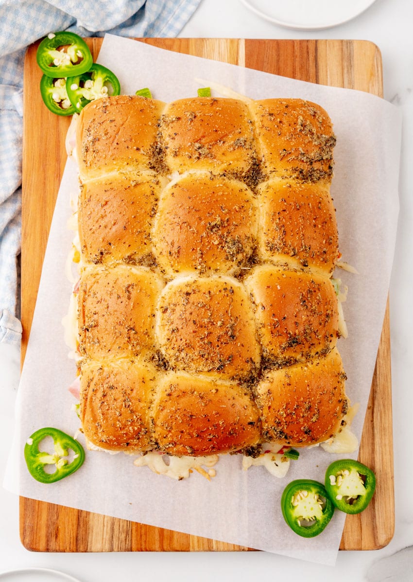 baked hawaiian pizza sliders on a parchment paper topped  wooden cutting board