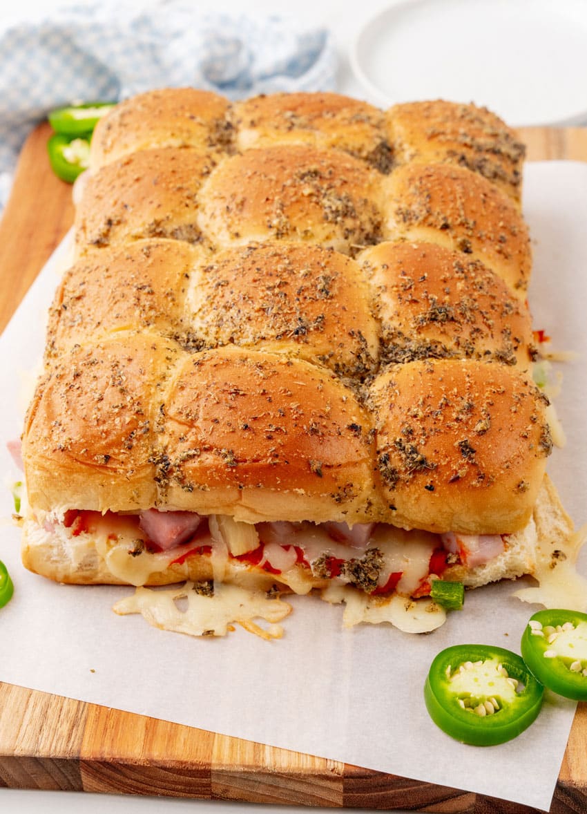 baked hawaiian pizza sliders on a parchment paper topped  wooden cutting board