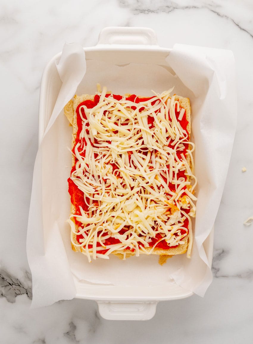 halved hawiian rolls topped with marinara sauce and shredded mozzarella cheese in a white baking dish