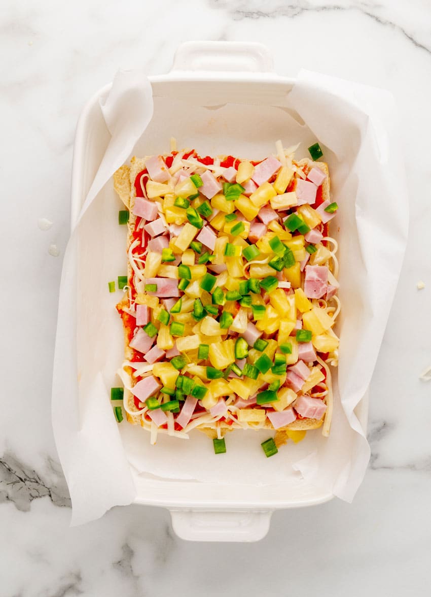 hawaiian pizza sliders in a parchment paper lined white baking dish