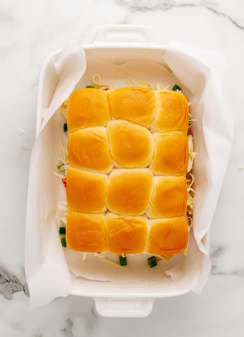hawaiian pizza sliders in a parchment paper lined white baking dish