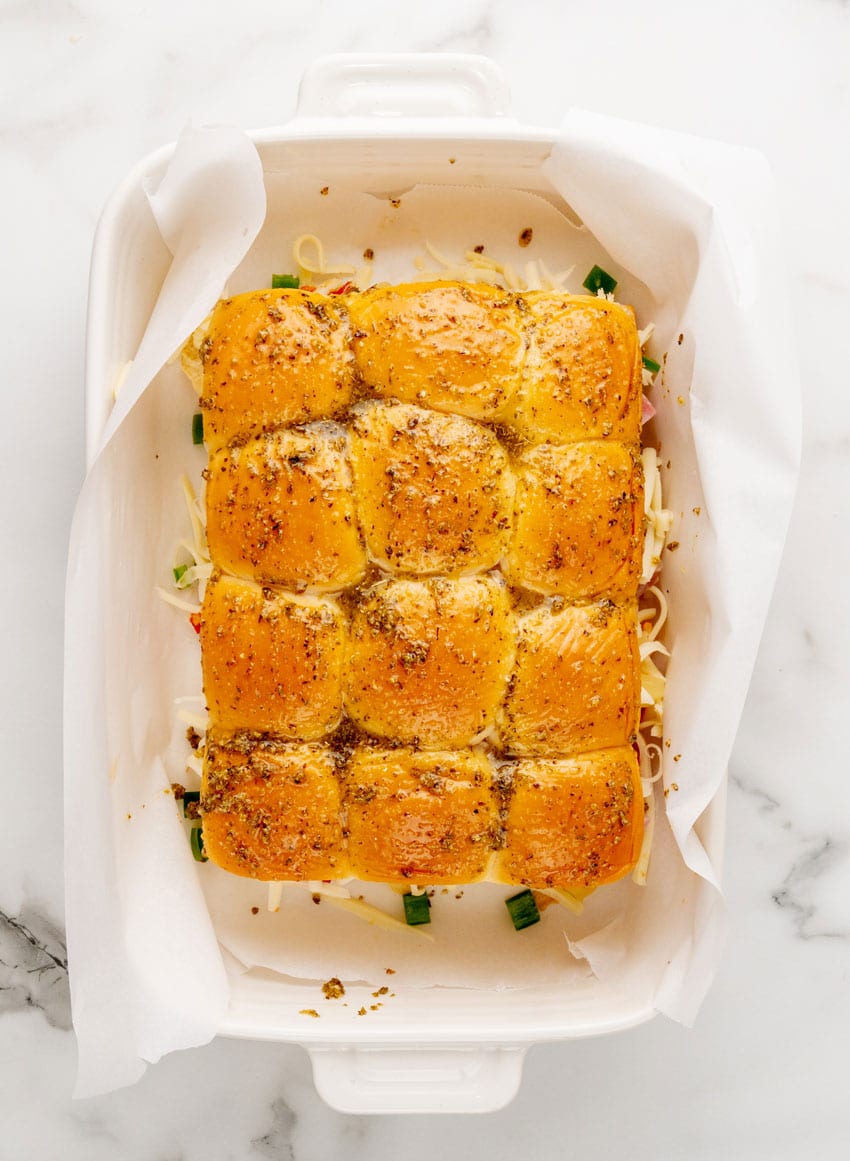 hawaiian pizza sliders in a parchment paper lined white baking dish
