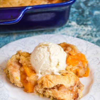 PEACH COBBLER DUMP CAKE ON A WHITE PLATE WITH A SCOOP OF VANILLA ICE CREAM ON TOP