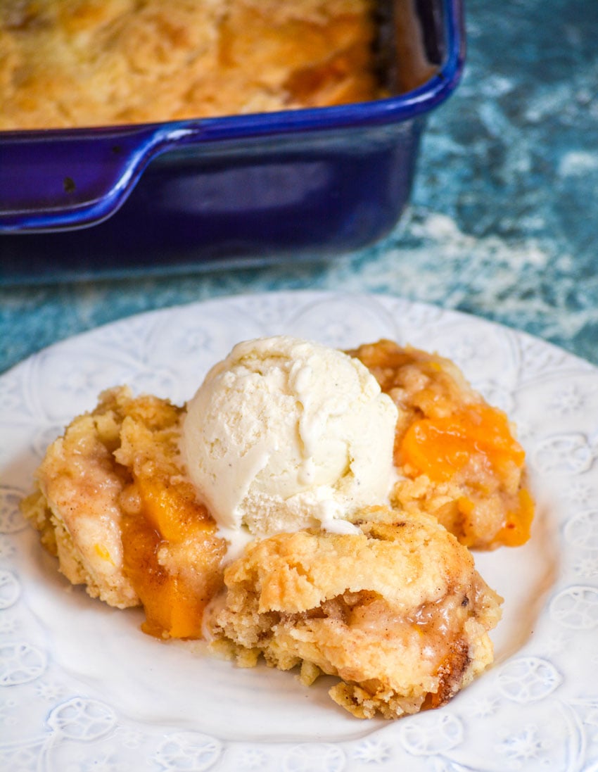 PEACH COBBLER DUMP CAKE ON A WHITE PLATE WITH A SCOOP OF VANILLA ICE CREAM ON TOP