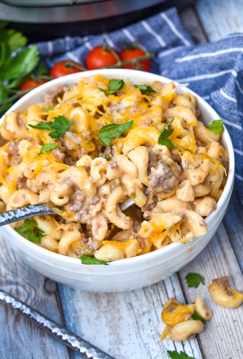 a silver fork stuck in a white bowl filled with instant pot cheeseburger pasta