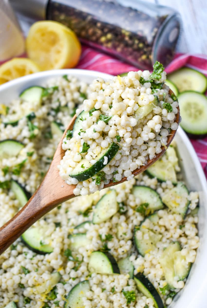 a wooden spoon holding up a scoop of cucumber couscous salad with lemon