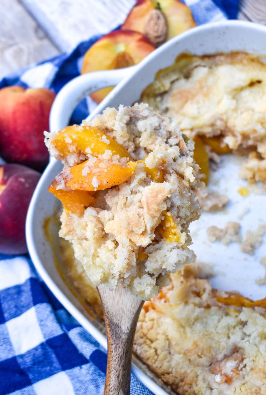 a wooden spoon holding up a scoop of dump and bake peach cobbler
