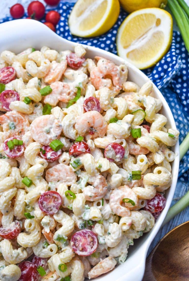 shrimp scampi pasta salad in a large white serving bowl with sliced lemons on the side