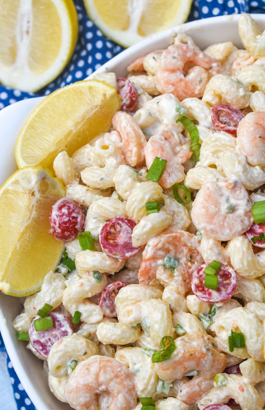 a closeup of shrimp scampi pasta salad in a white serving bowl with two lemon wedges on the side