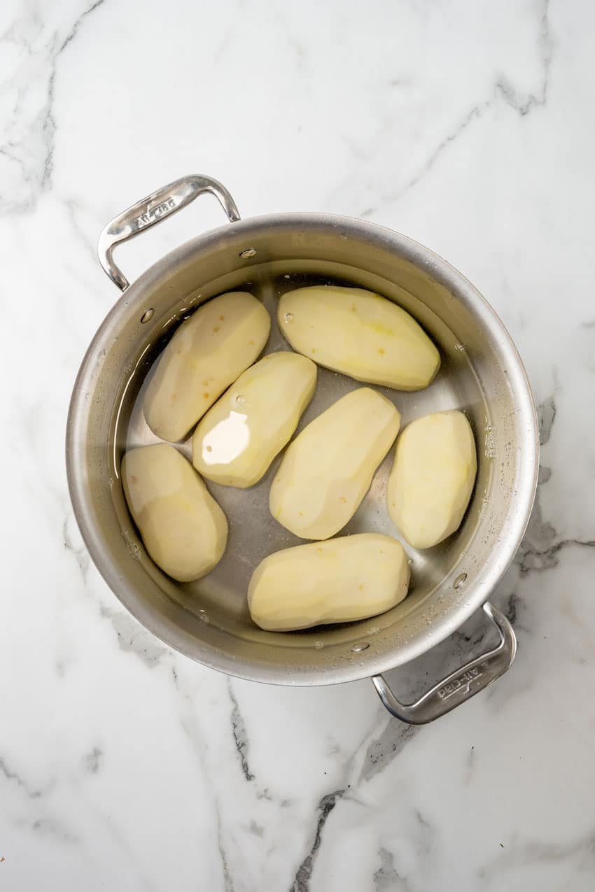 peeled potatoes covered in water in a steel pot