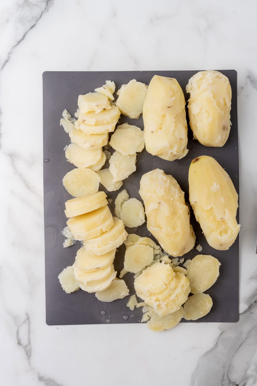 sliced boiled peeled potatoes on a black cutting board