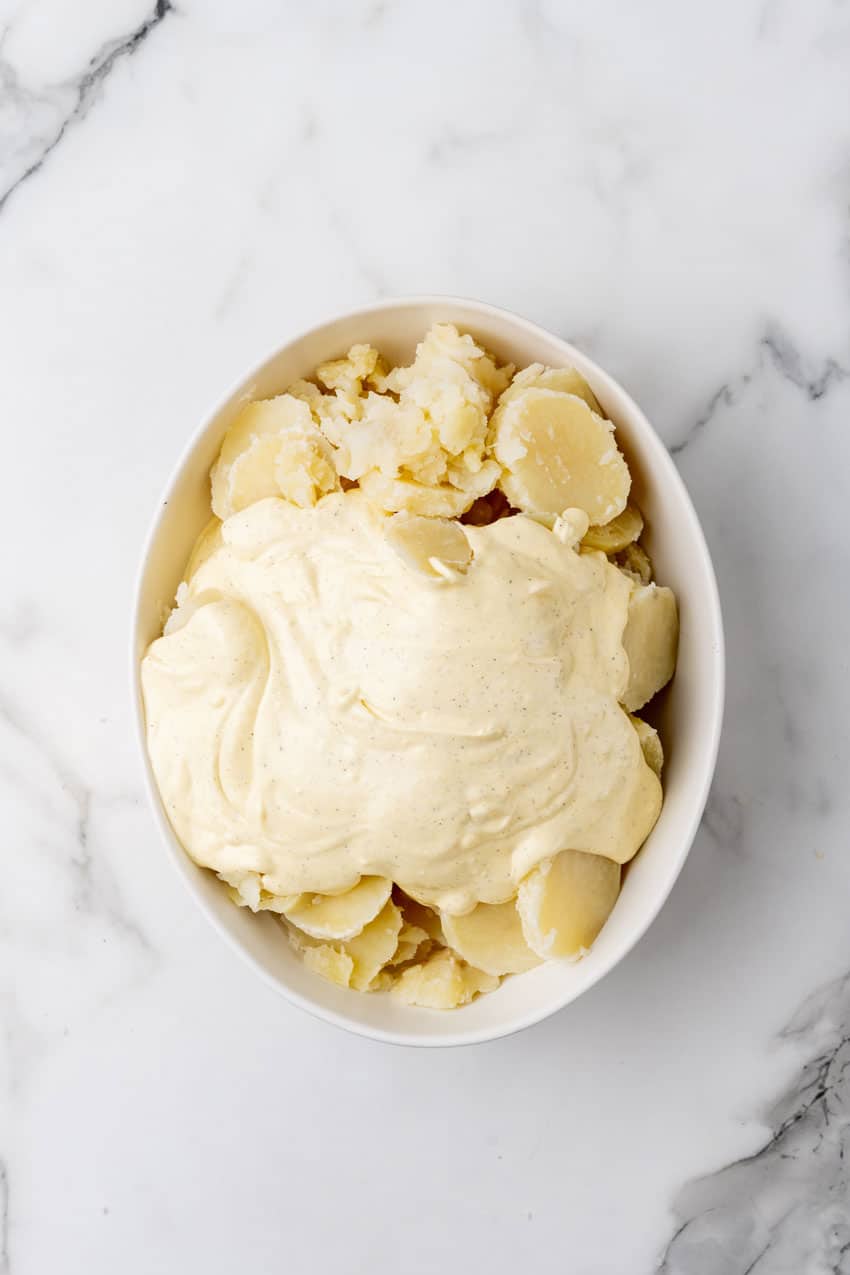 sliced boiled peeled potatoes covered in salad dressing in a white serving bowl
