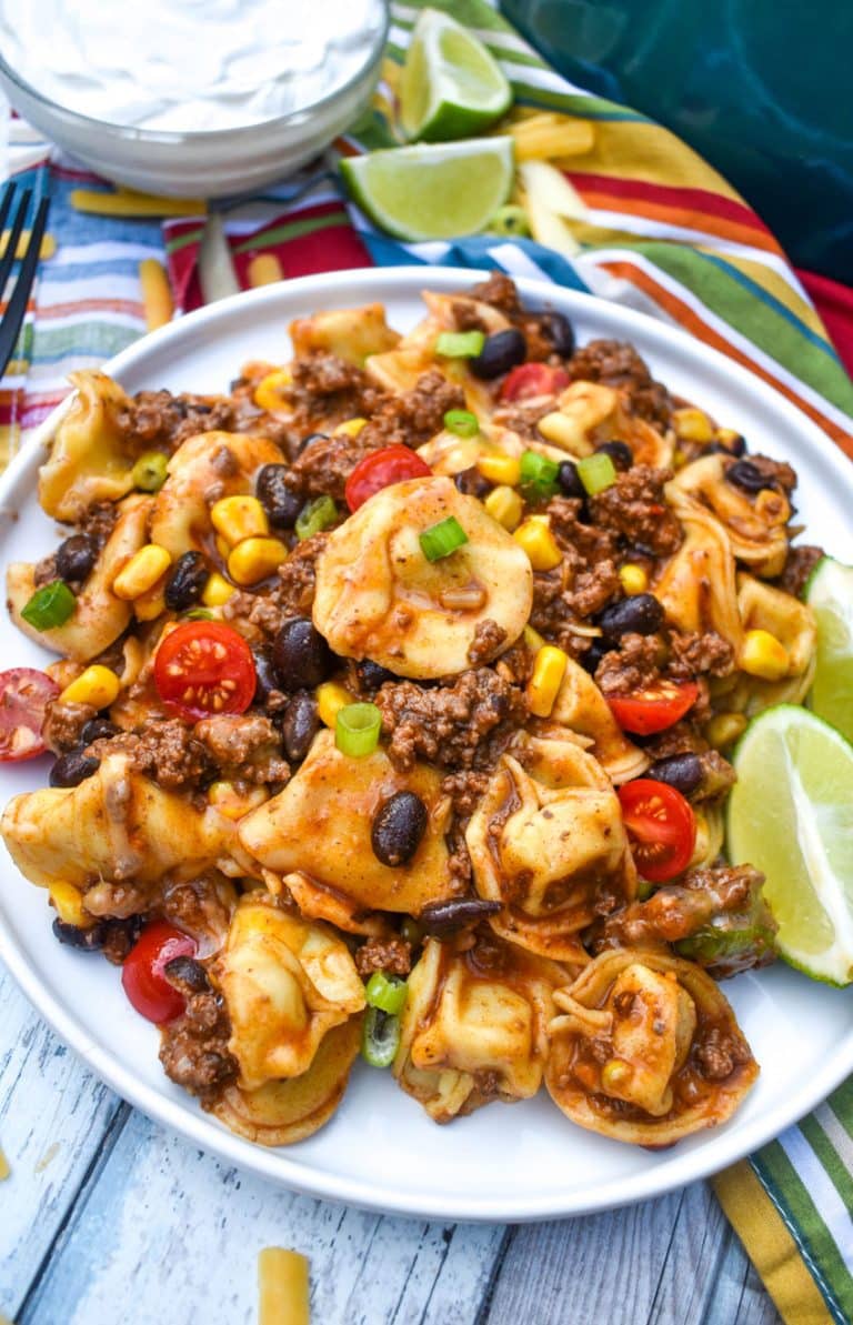 taco tortellini served on a white dinner plate with fresh lime wedges on the side