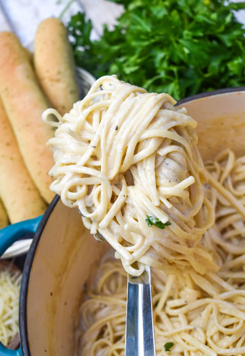 a silver ladle holding up a scoop of creamy garlic parmesan pasta