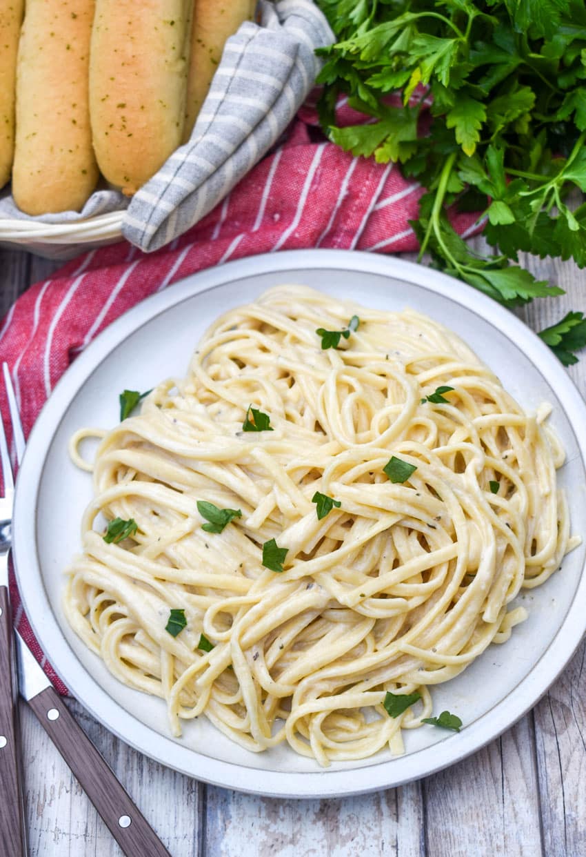creamy garlic parmesan pasta topped with fresh parsley leaves on a white plate