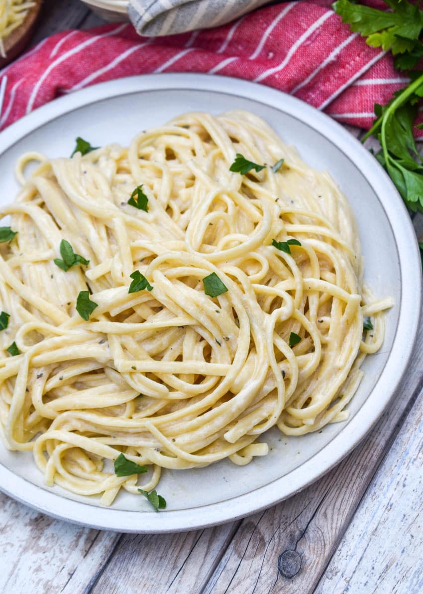 creamy garlic parmesan pasta topped with fresh parsley leaves on a white plate