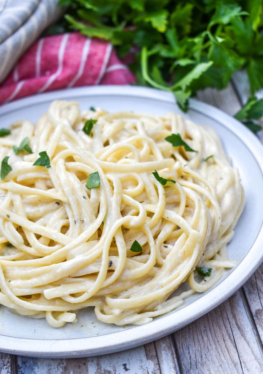 creamy garlic parmesan pasta topped with fresh parsley leaves on a white plate