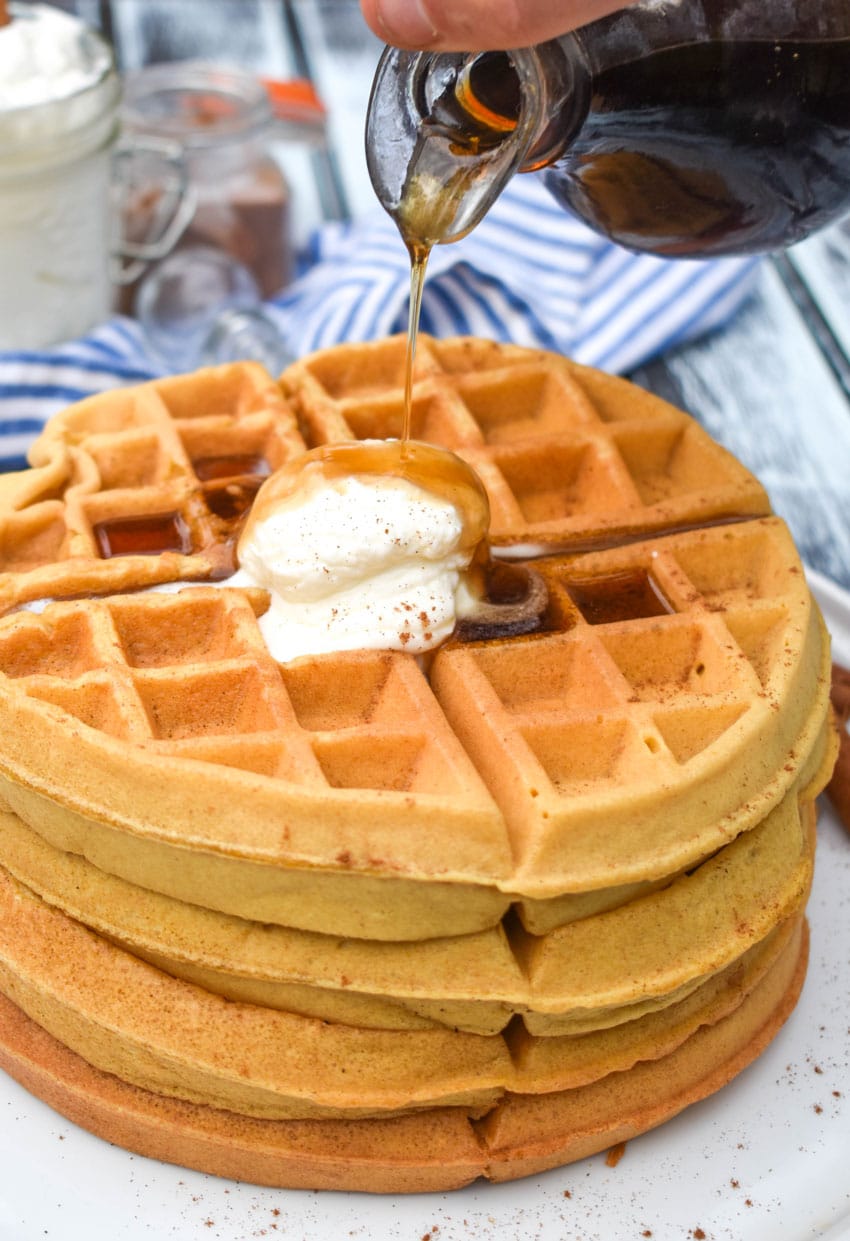 syrup being poured over a stack of pumpkin spice waffles on a white plate