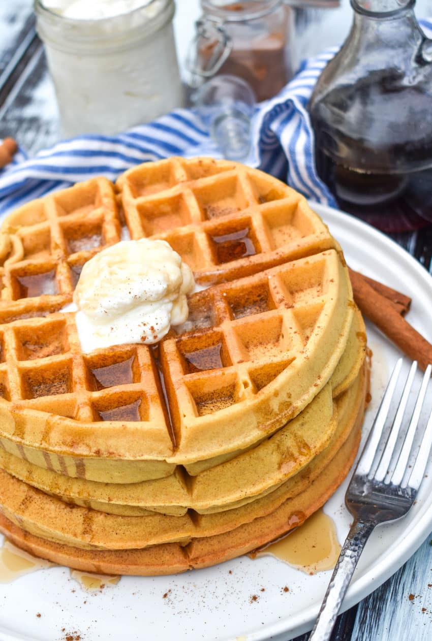 a stack of syrup covered pumpkin spice waffles on a white plate