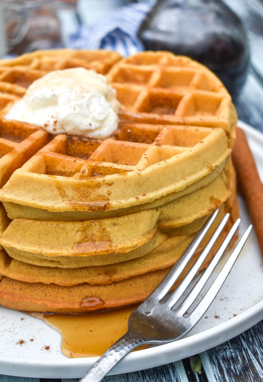 a stack of syrup covered pumpkin spice waffles on a white plate