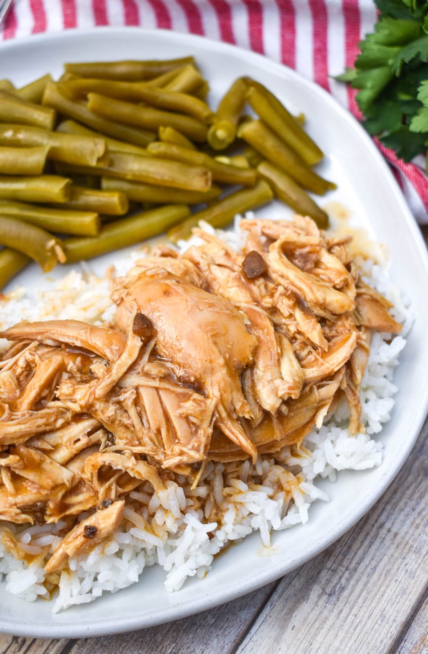 crockpot chicken and gravy over steamed white rice on a white dinner plate