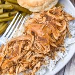 crockpot chicken and gravy over steamed white rice on a white dinner plate