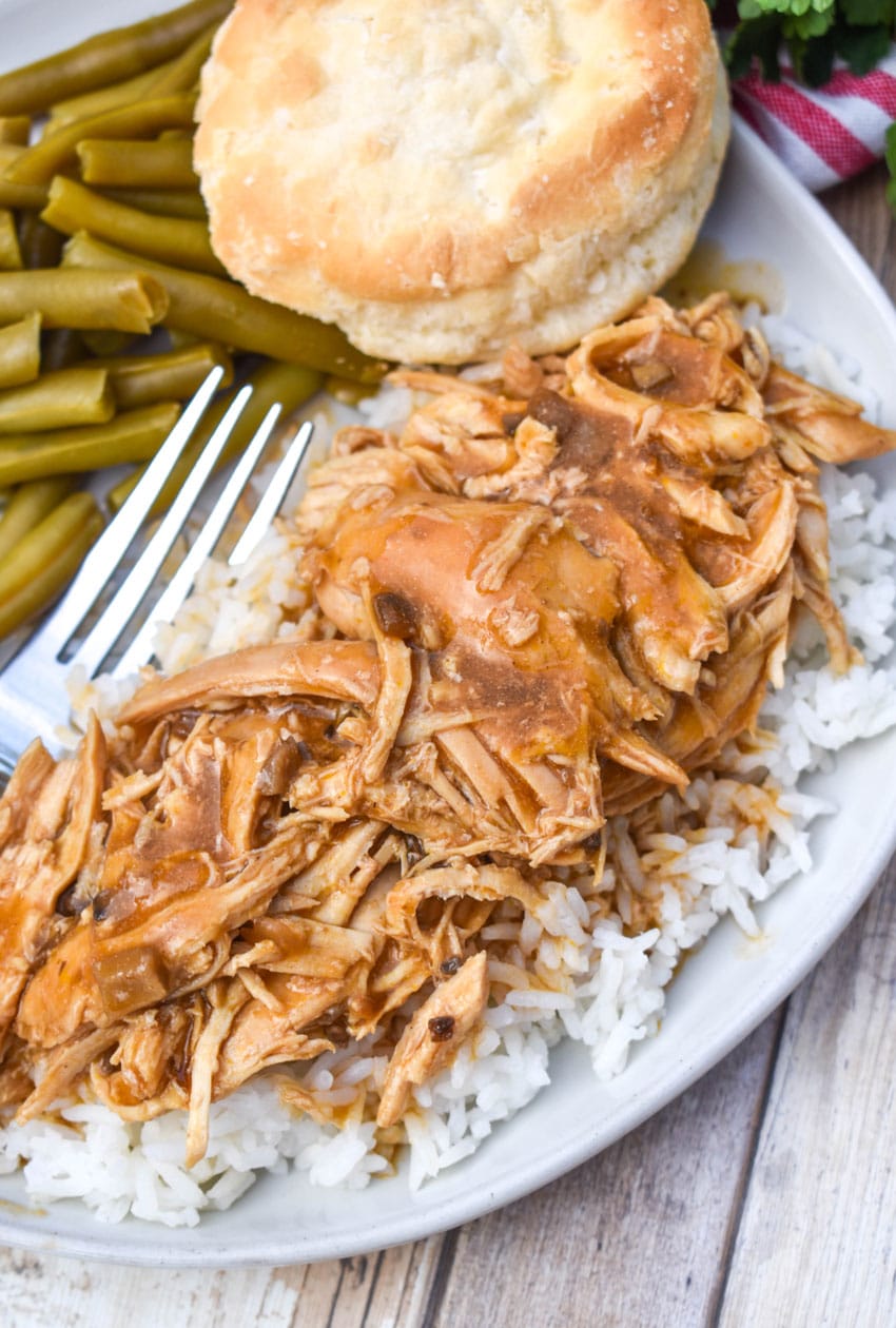 crockpot chicken and gravy over steamed white rice on a white dinner plate